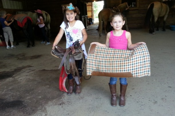 Two young girls holding saddle pads in a barn