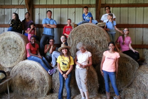 Group of children and adults standing in front of hay bales in a barn