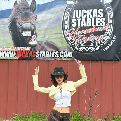 Person in cowboy attire points to 'Juckas Stables Horseback Riding' sign with a photo of a smiling horse.