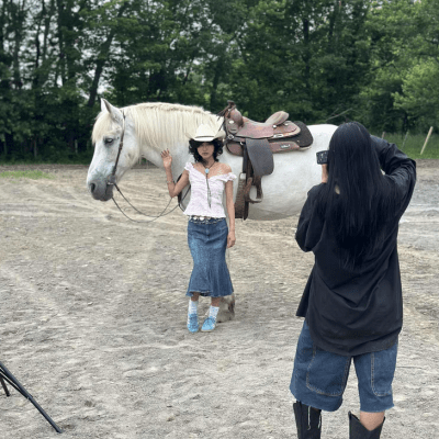 Person in cowboy hat poses with white horse while another person takes a photo in an outdoor setting.