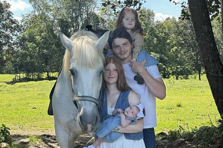 Family of four and a horse in a sunny park with trees.