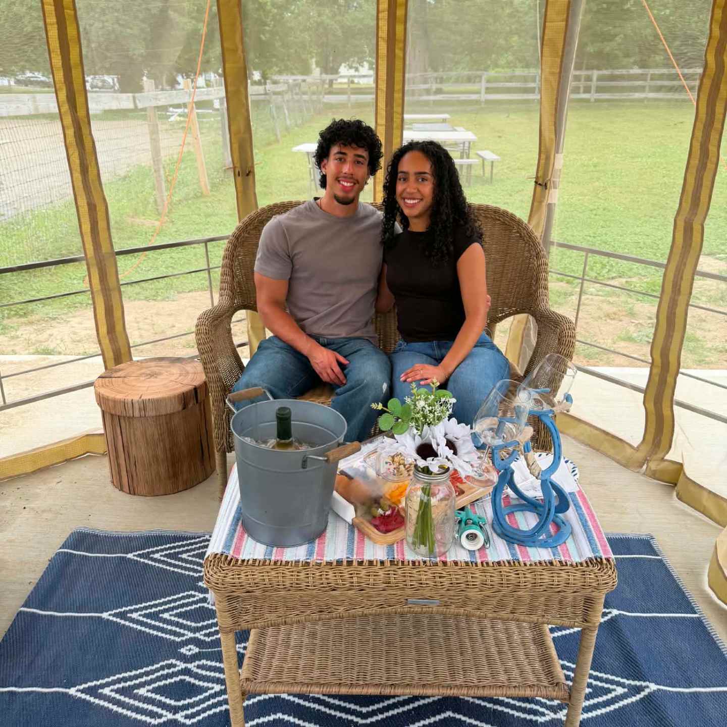 Couple sitting in a gazebo with a wicker table and decorative items outside.