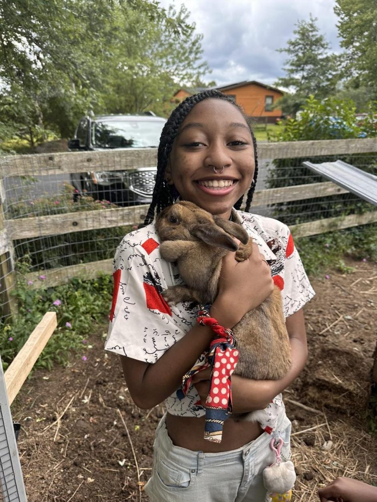 Person smiling while holding a brown rabbit outside near a wooden fence.
