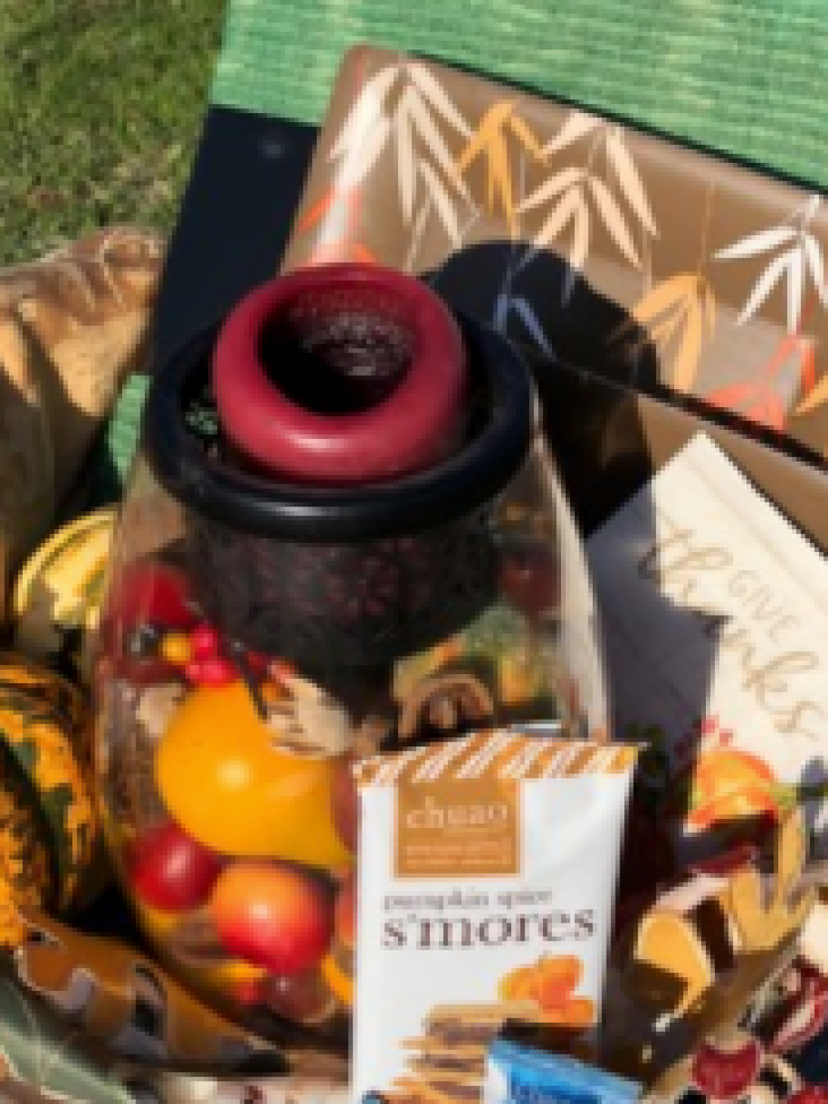 Autumn-themed basket with gourds, chocolates, candle, and fall decorations on a sunny day.