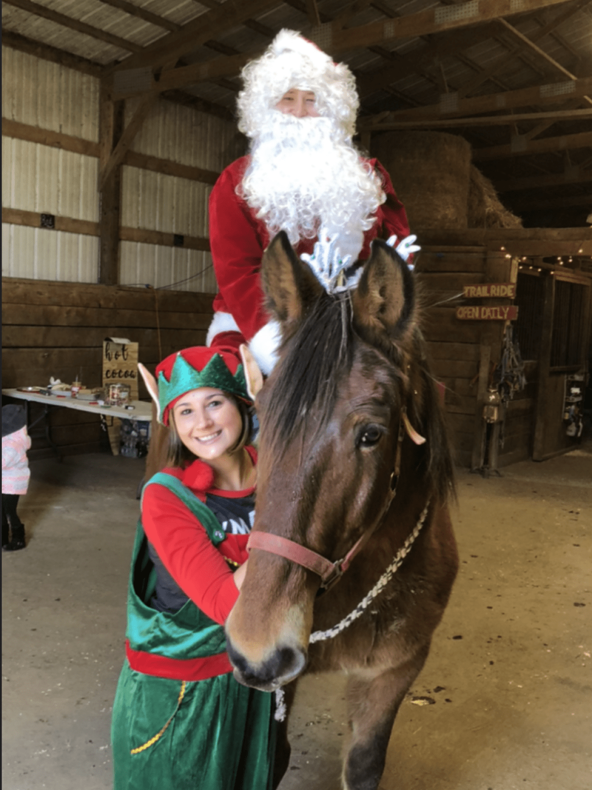 Santa on a horse with an elf in a barn.