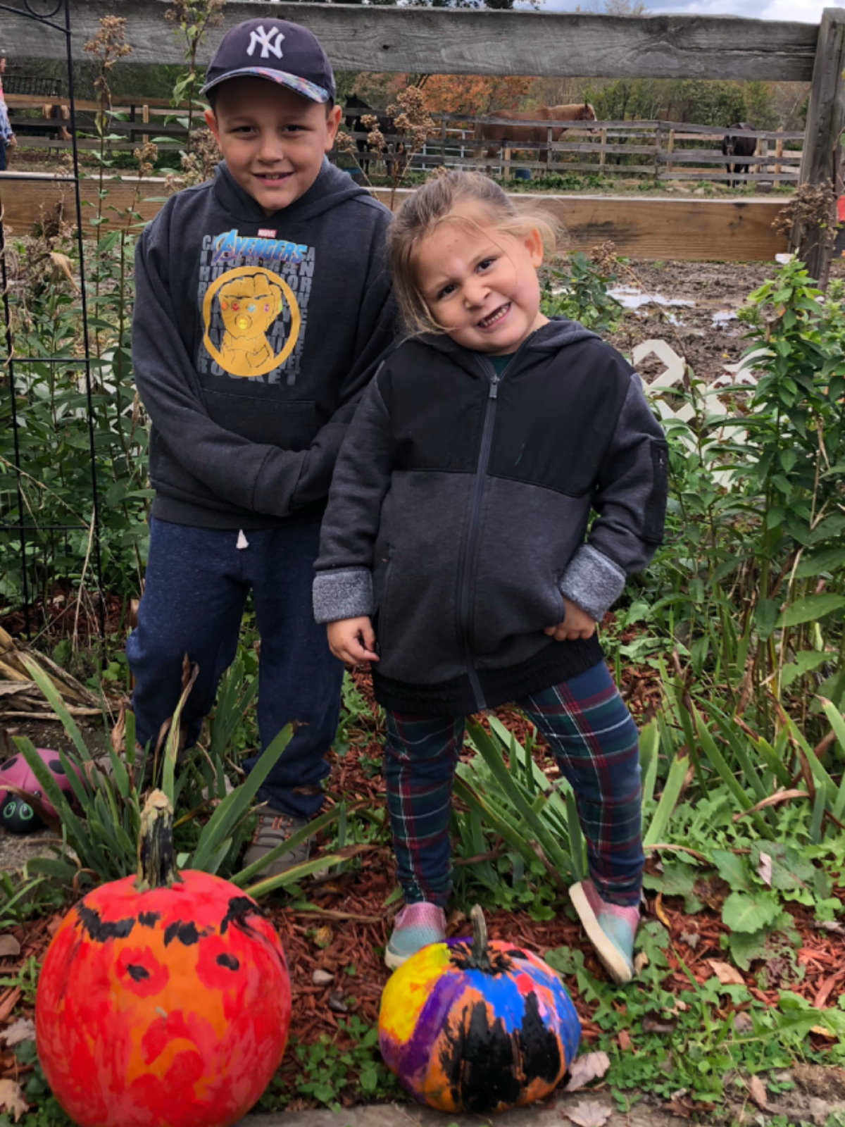 Two children smiling with painted pumpkins in a garden setting.