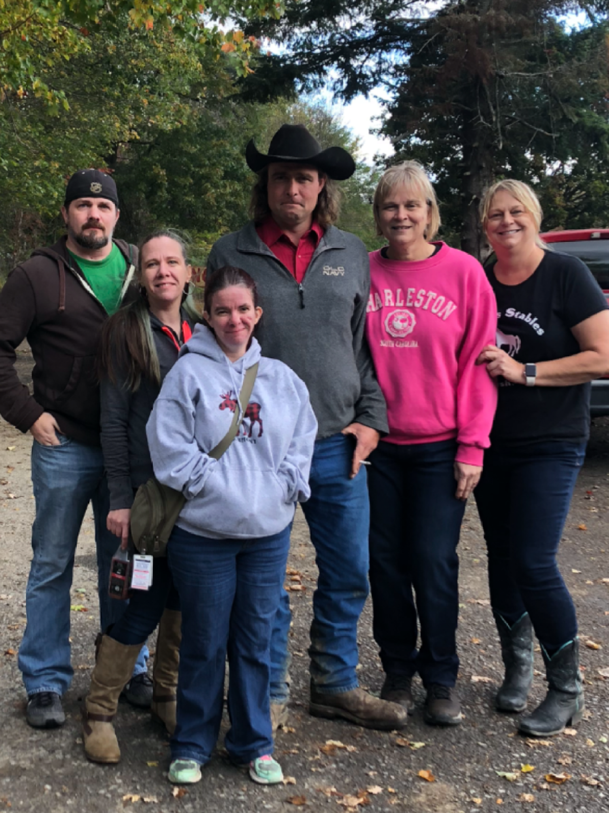 Group of six people posing outdoors, some wearing casual jeans and boots.