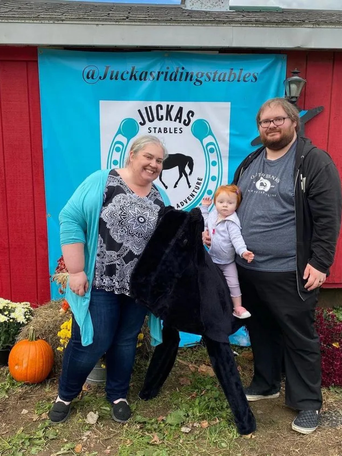 A family posing with a stuffed horse in front of a red wall with a horse stable sign.