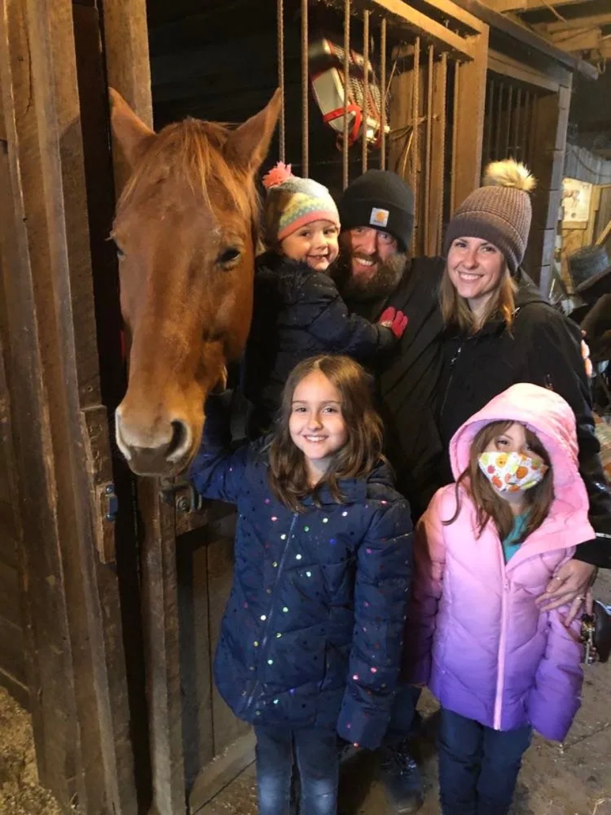Family posing with a horse in a barn, wearing winter clothing.