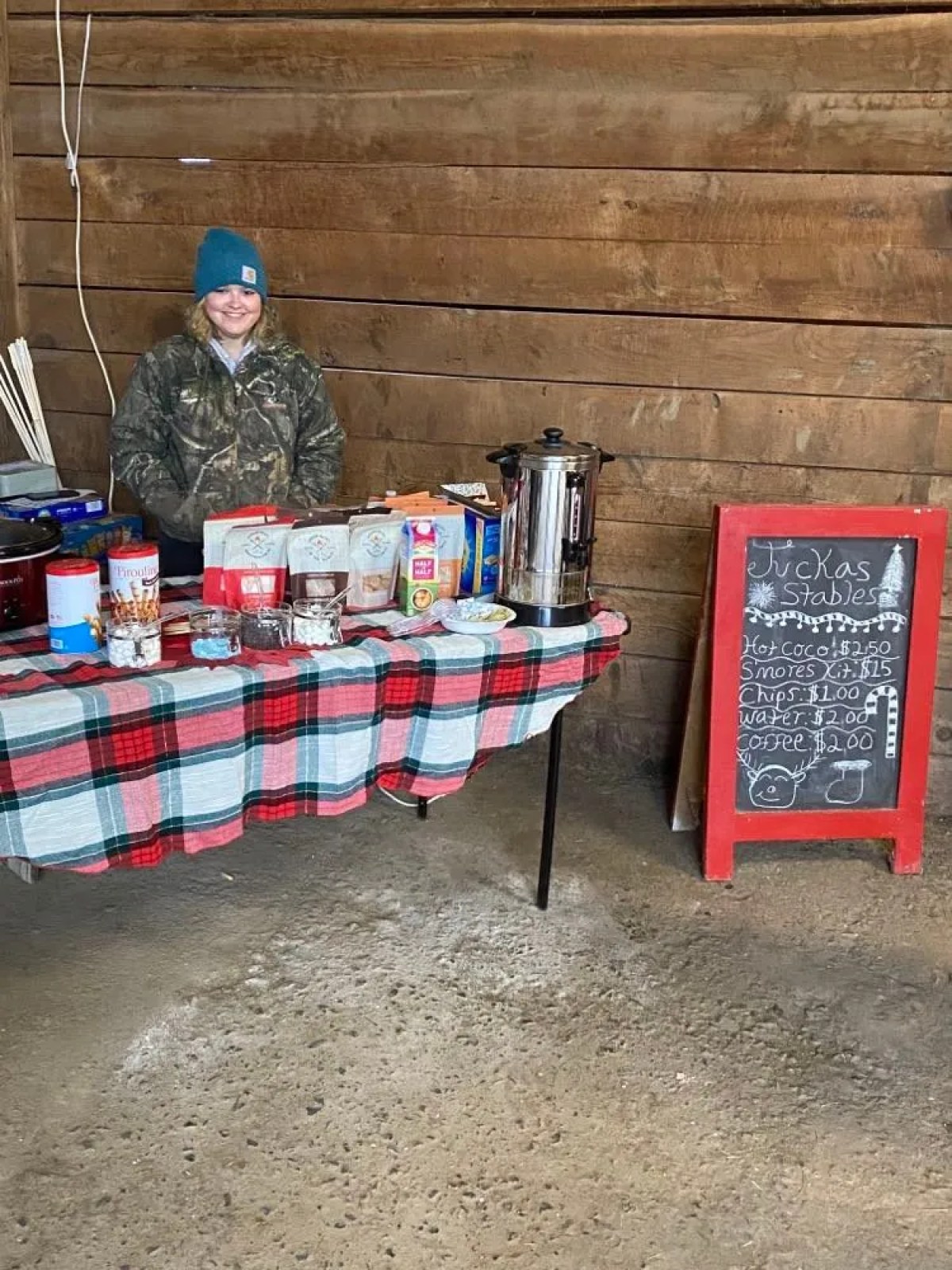 Person in beanie at cozy snack stand with chalkboard menu beside them.
