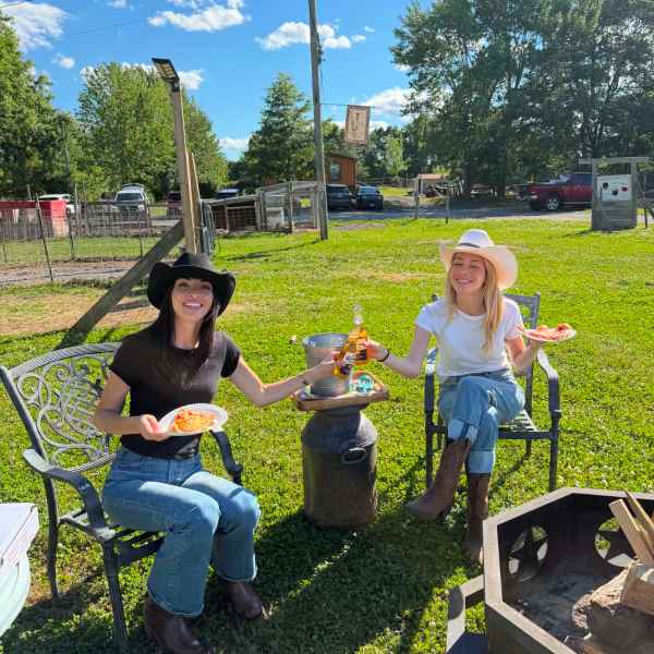 Two women in cowboy hats eating outdoors on a sunny day.
