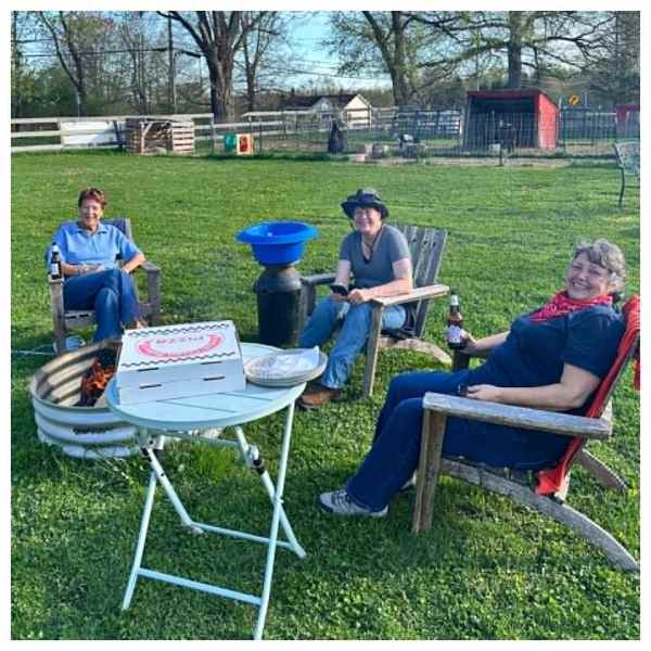 Three people sitting outside with pizza and drinks near a fire pit.