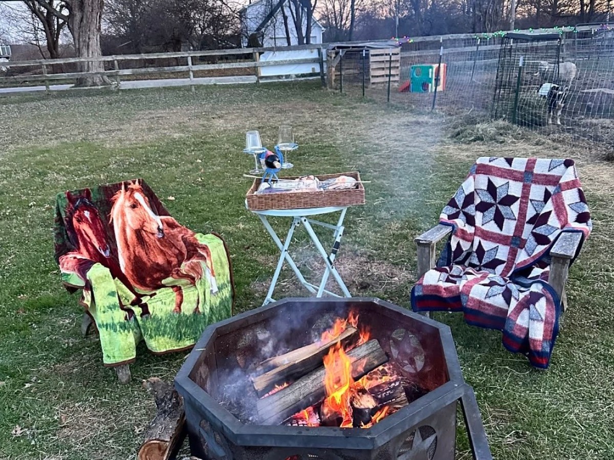 Outdoor fire pit with two chairs, blankets, and a small table in a grassy yard.